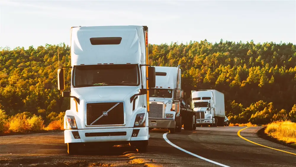 Row of semi-trucks driving on a forested highway